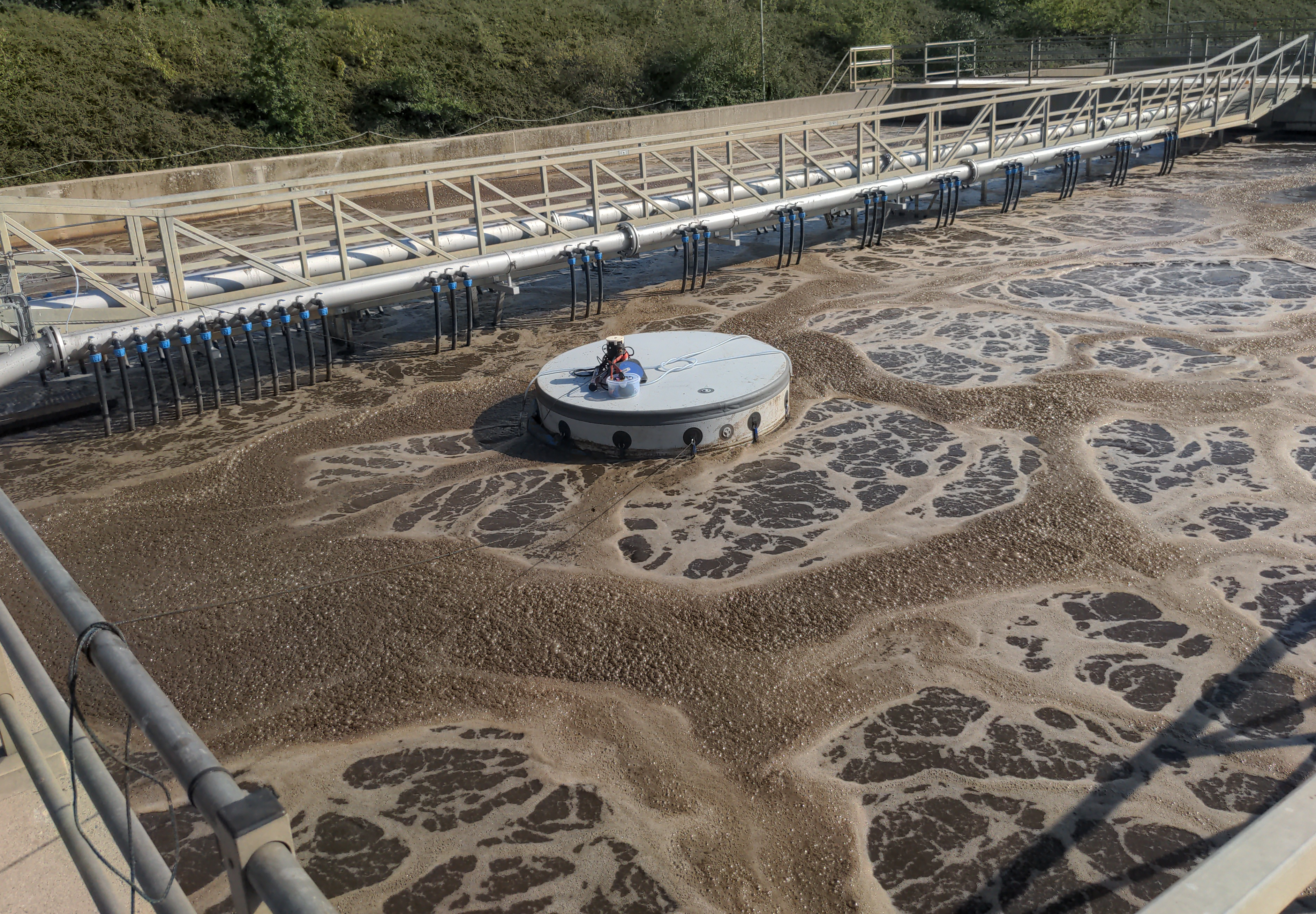 Eine Fotografie unserer Ablufthaube. Es ist ein Becken einer Kläranlage von oben abgebildet. Das Becken ist mit braunem Abwasser gefüllt. Auf dem Wasser schwimmt eine pyramidenförmige Konstruktion, die unsere Messtechnik zur Abluftuntersuchung enthält.